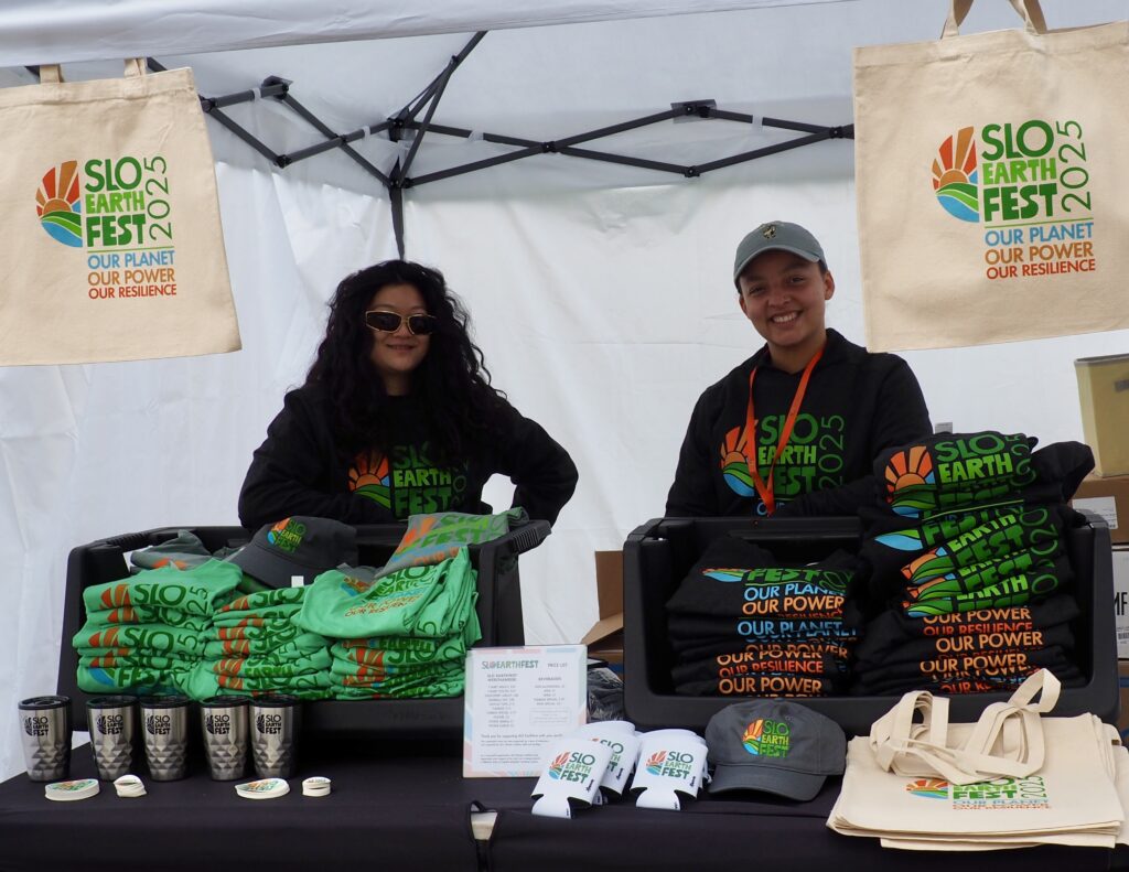 Two volunteers at SLO EarthFest booth with eco-friendly merchandise.